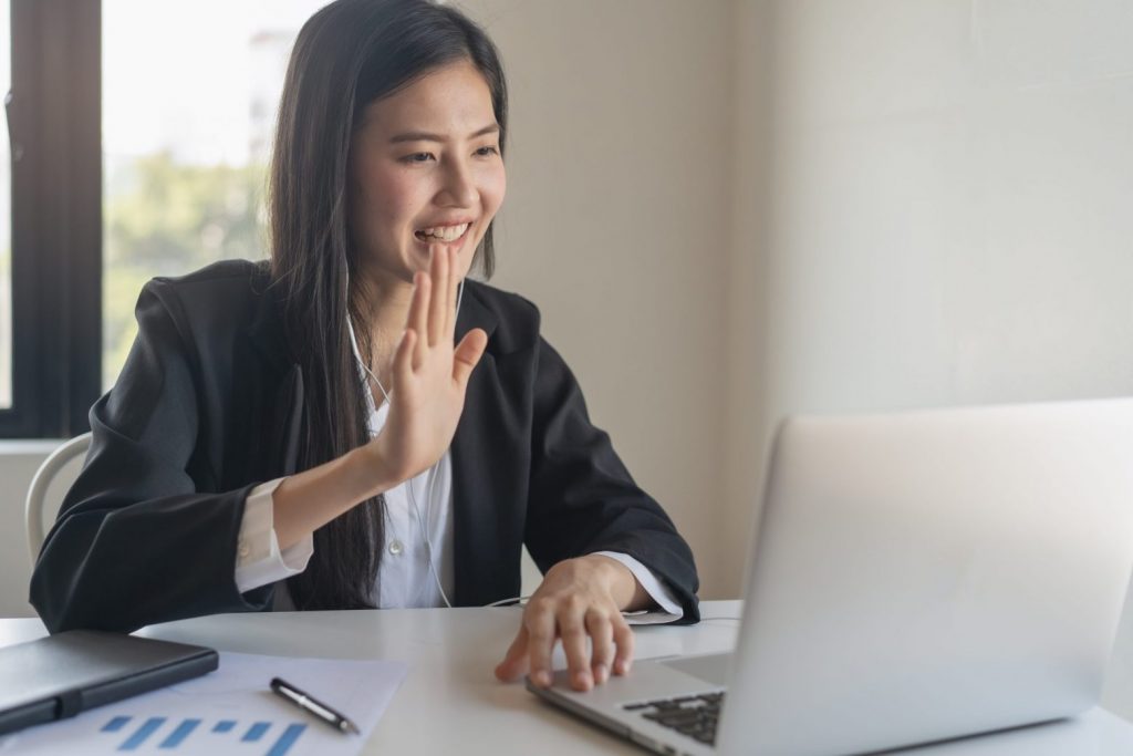 Happy young asian business woman waving hands to greeting partner during making video conference with her team. job interview