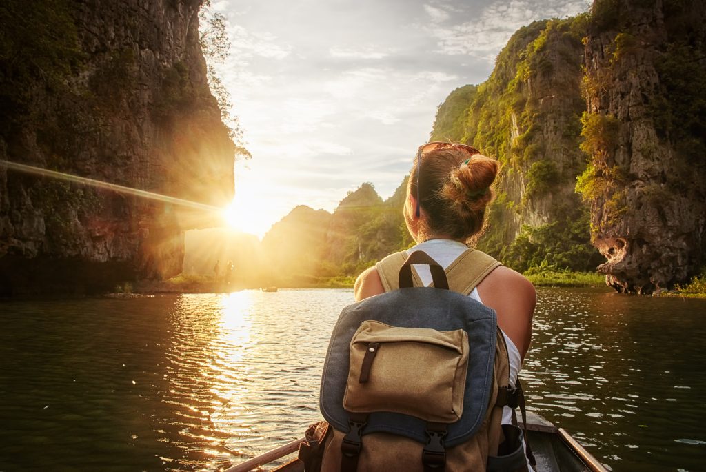 Happy woman with backpack traveling by boat enjoying sunset among of karst mountains in the North of Vietnam. TEFL