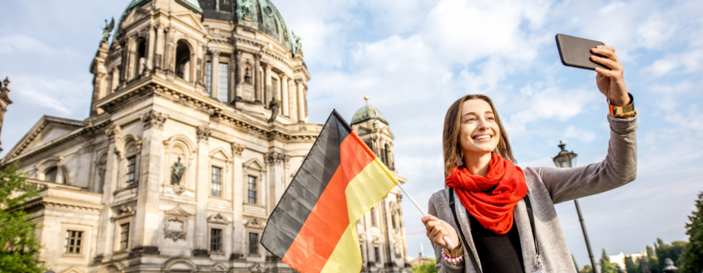 Irish teacher taking a selfie with a German flag in front of a historic cathedral, getting ready to teach English in Germany from Ireland