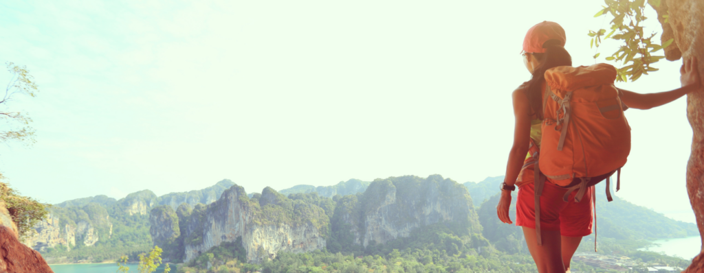 Backpacker standing on a cliff edge overlooking tropical mountains and sea, symbolising the freedom to move abroad from Ireland and teach English overseas.