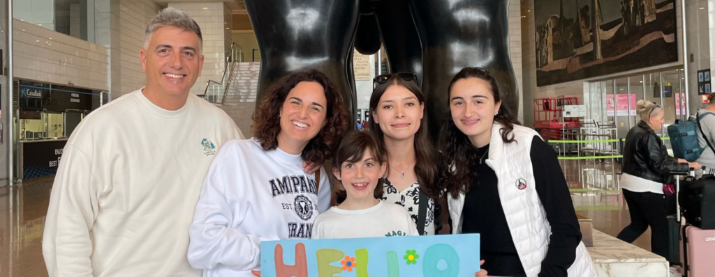 Family welcoming an English teacher abroad with a colourful “hello” sign at the airport, illustrating how teaching English overseas creates warm connections even when you don’t speak another language.