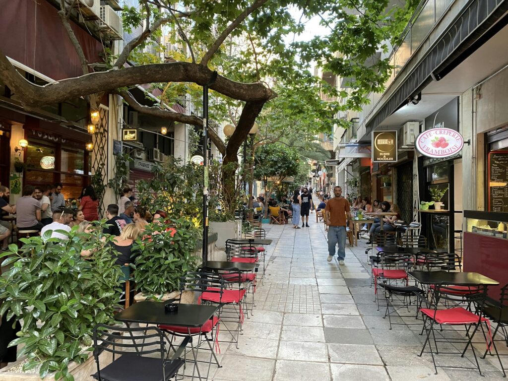 Pavement cafés and restaurants lining a busy Athens street in the late afternoon