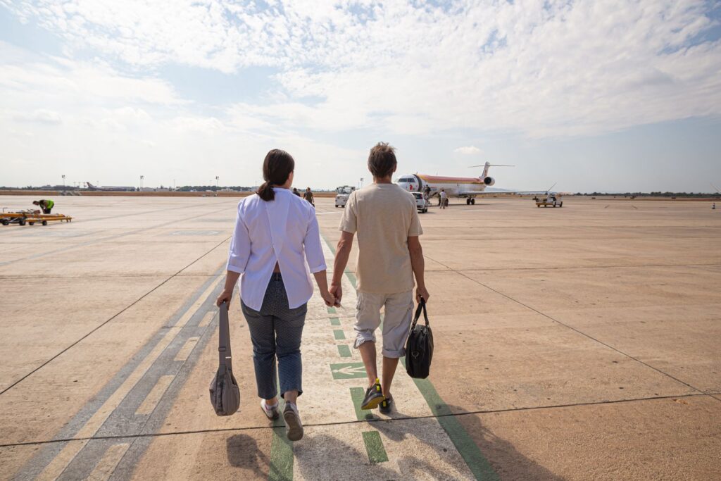 A couple holding hands walking towards a plane at the airport
