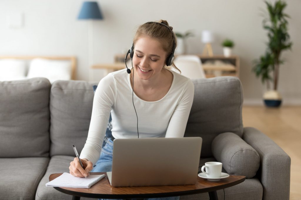 Happy girl interpreter in headset write notes study on laptop