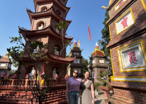 Two TEFL teachers abroad smiling in front of historic brick pagodas on a sunny day, discovering local traditions in Vietnam
