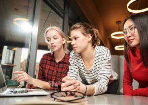 Three adults working together on a laptop, planning how to teach English online without a degree in a shared workspace